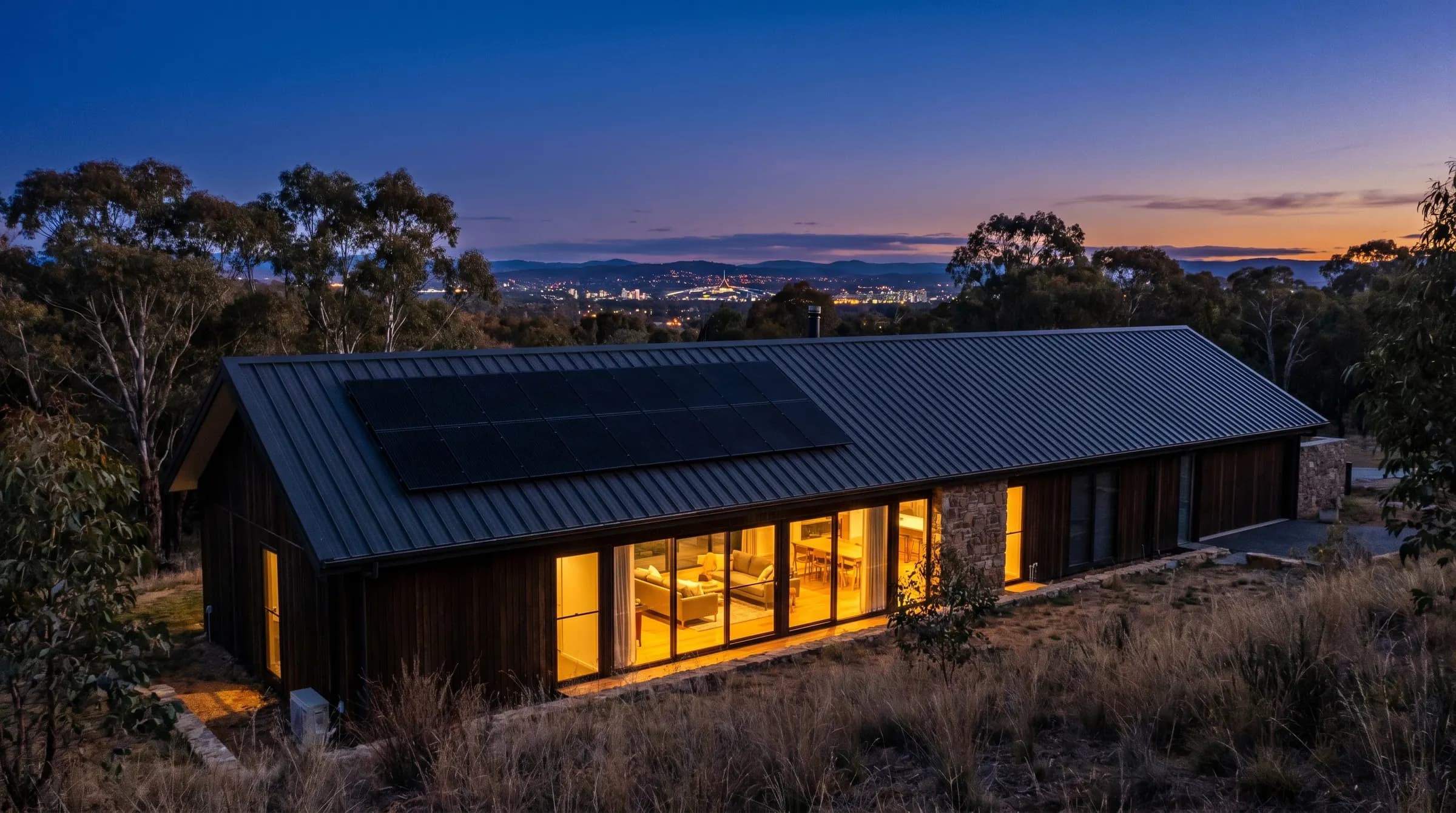 All-black solar array flush on a dark steel roof, Canberra bushland and city lights beyond at dusk